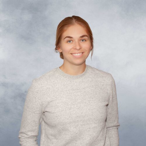 Sarah poses for photo, in front of a heathered periwinkle backdrop.