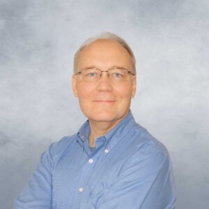 Michael Glod smiles for his portrait in front of a heathered periwinkle backdrop